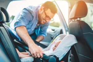 father putting his baby boy on a safety child car seat