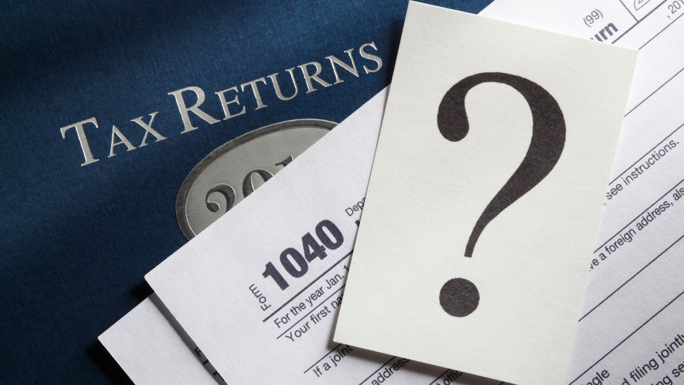 Question mark over tax forms and returns, symbolizing uncertainty about tax obligations. Do you have to pay taxes on personal injury settlements in Texas?